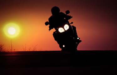 Fototapeta premium silhouette of rider on a motorbike driving at sunset - space for your text