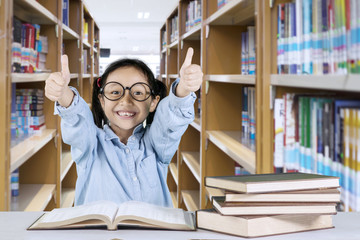 Cute schoolgirl showing thumbs up in the library