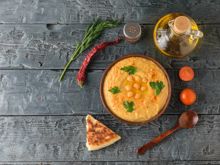 Bowl with fresh hummus, olive oil, chili and cherry tomatoes on a dark rustic table. The view from...