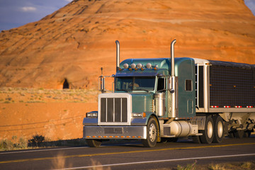 Classic big rig semi truck with low bulk covered semi trailer transporting cargo on the road in Page Arizona