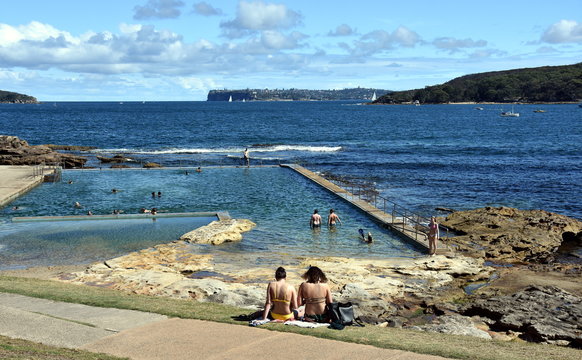 Fairlight beach on a sunny day in summer. People enjoy the cool water in Fairlight Tidal Swimming pool. South Head and Dobroyd Head in the background.