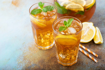Traditional iced tea with lemon, mint and ice in tall glasses. Two glasses with cool summer drink on old rusty background. With copy space