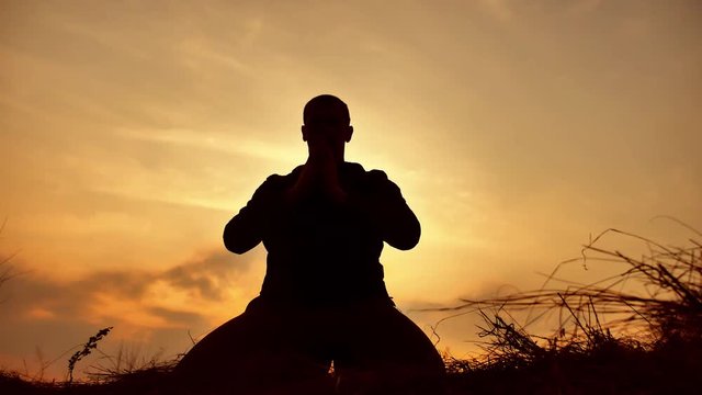silhouette of a male monk engaged in meditation at sunset sunlight. Buddhist prays at sunset healthy way lifestyle of life nature