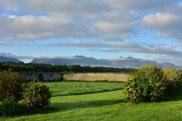 Fresh green meadows surrounded by stone walls with hills blending with clouds in far background in countryside of County Kerry in Ireland.