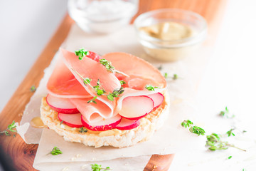 Crisp bread healthy snack with Parma ham, radish slices, mustard, sea salt and fresh thyme. Easy breakfast close-up on a white background with copy space.