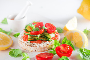 Crisp bread healthy snack with salmon, cottage cheese, cucumber stripes, fresh cherry tomatoes, mint, lemon juice, pepper. Easy breakfast close-up on a white background with copy space.