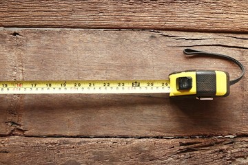 Yellow measuring tape on wood background