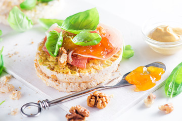 Crisp bread healthy snack with Parma ham, walnuts, mustard, apricot jam, fresh basil leaves. Easy breakfast close-up on a white background with copy space.