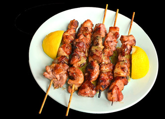 souvlaki in a plate with slice of lemon isolated in black