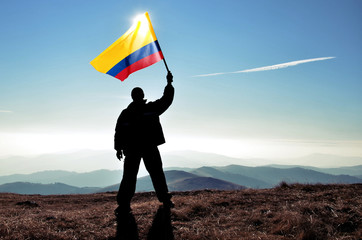 Successful silhouette man winner waving Colombian flag on top of the mountain peak