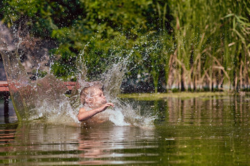 Young boy jumping, swimming and splashing in the river on summertime