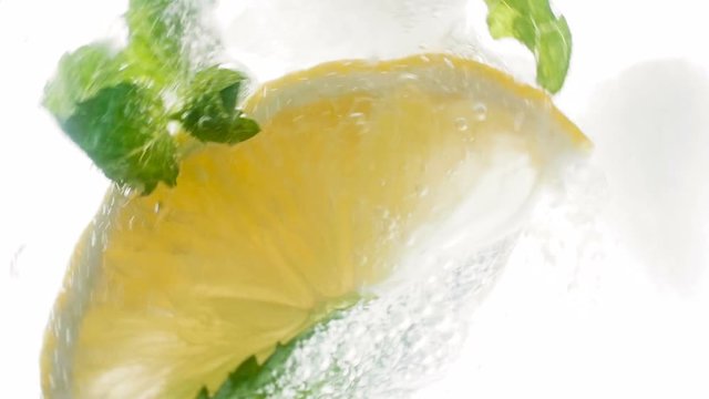 Clooseup slow motion footage from high point of throwing ingredients of lemonade or mojito cocktail in glass