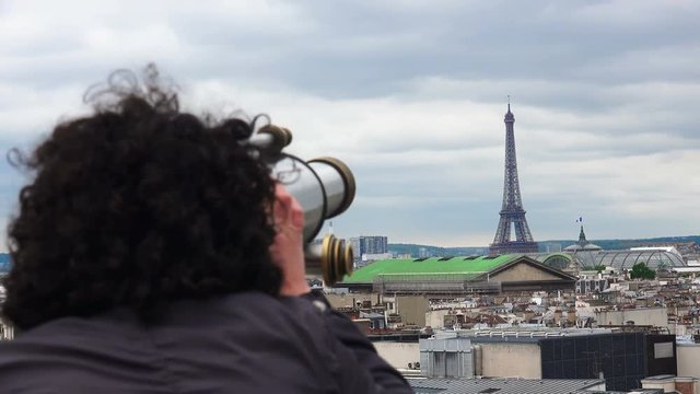 Beautiful girl looking through coin operated binocular on terrace of Laffaete Galery in Paris, France. View of Eiffel Tower and Opera Garnier at background