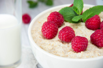 fresh delicious oatmeal with raspberries and mint, next to a mug with milk, a healthy diet, a nutritious breakfast