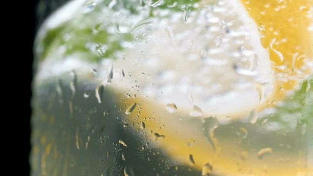 Macro slow motion footage of water prolets on cold glass of lemonade against black background