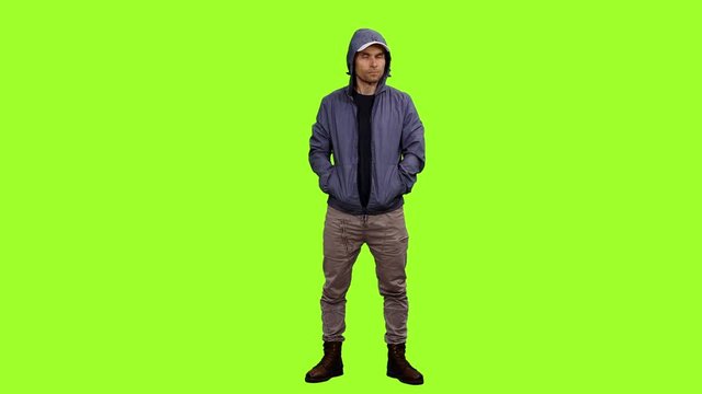 Front view of hooded man standing with hands in pockets on green background, Chroma key
