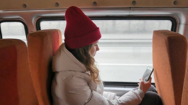 young cheerful woman in a red hat, traveling by bus on a sad day. She takes pictures on a smartphone