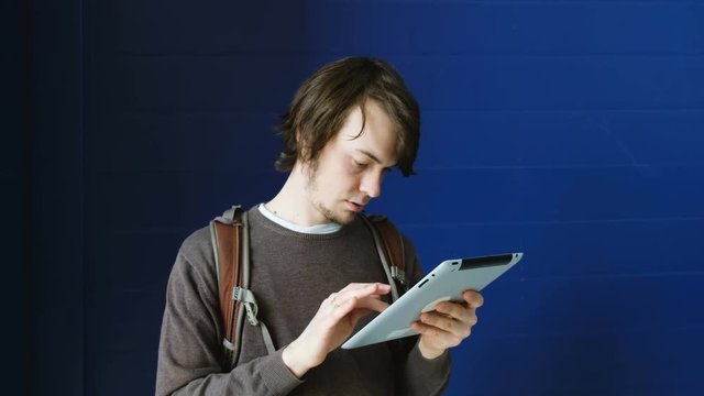 Young business man uses a tablet on a blue wall background