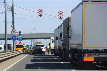 The queue of trucks with semi-trailers to the control point in the spring against the blue sky, inspectors in yellow jackets and camouflage check the documents of the driver of the car