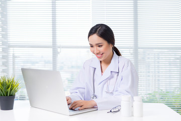 Fototapeta na wymiar Young smiling female doctor sitting at office desk and working with a laptop
