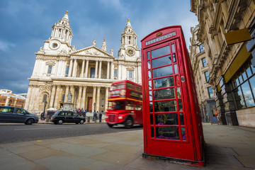 London, England - Traditional red telephone box with iconic red vintage double-decker bus on the move at St.Paul's Cathedral on a sunny day