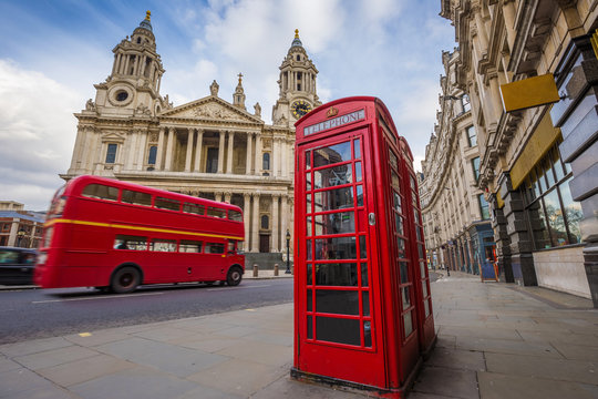 London, England - Traditional red telephone box with iconic red vintage double-decker bus on the move at St.Paul's Cathedral on a sunny day