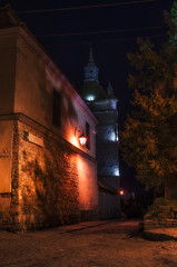Stone sidewalk, aged building with retro lantern and church on the street in the old city at night