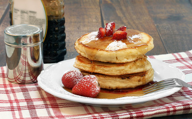 Pancakes with fresh strawberries, powdered sugar and maple syrup.