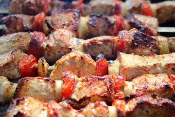 Pieces of juicy slices of marinated pork meat strung on skewers with slices of chopped tomatoes and onion cooking on barbecue. Cooking shashlik on the brazier