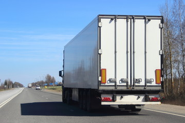 Transportation logistics - white semi trailer truck on asphalt road in summer on blue sky background, rear view