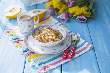 a cup of fragrant coffee and porridge with a quince. A healthy and delicious breakfast. A bouquet of spring bright tulips and sunlight. Blue wood background. Free method for text
