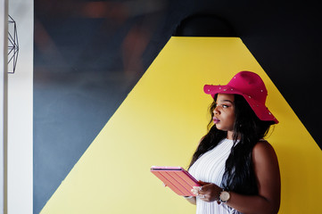 African american woman in hat with tablet at hands against black and yellow futuristic wall.