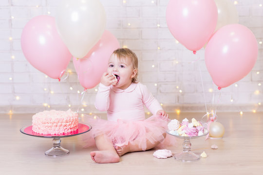 birthday party concept - funny little girl eating cake over brick wall background with lights and balloons