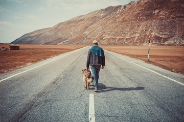 man walking on the road with his dog in the mountains - obrazy, fototapety, plakaty