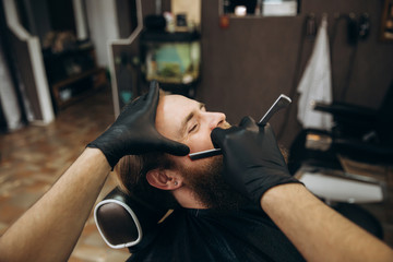 Bearded man with long beard getting stylish hair shaving , haircut , with razor by barber in barbershop