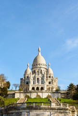 Fototapeta na wymiar The basilica of the Sacred Heart of Paris under a blue sky in springtime seen from the bottom of the Louise Michel park, with the terrace and stairways on the foreground.