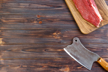 fresh large piece of pork on a wooden cutting board with kitchen ax. Top view on gray concrete background