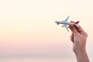 Woman hand holding airplane model in sunset sky and summer sea background dreams of journey in vacation.