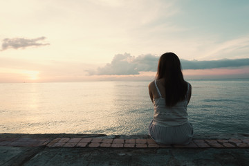 Silhouette of young woman sitting alone on back side outdoor at tropical island beach missing...