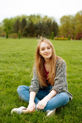 Cheerful young blonde woman sitting on grass in park