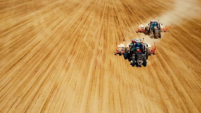 Aerial drone shot of a farmers in two tractor seeding, sowing agricultural crops at field