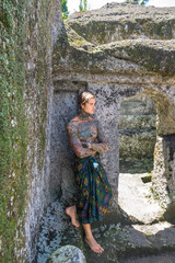 shirtless tattooed man standing at ruins in bali, indonesia