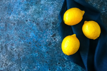 Three ripe yellow lemons on a blue stone background. Top view and copy space.