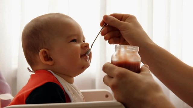 Young happy father feeds his son baby fruit puree.