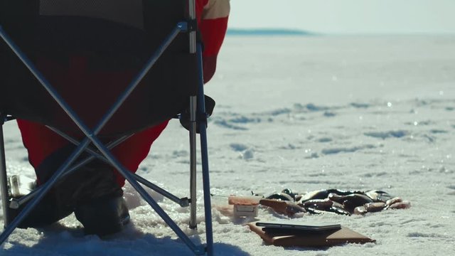 Man angler fishing on winter lake and putting successful caught fish in ice