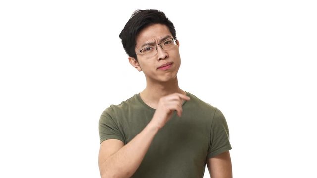 Portrait of brunette chinese man wearing glasses and basic t-shirt doing shh gesture with index finger on lips, isolated over white background. Concept of emotions