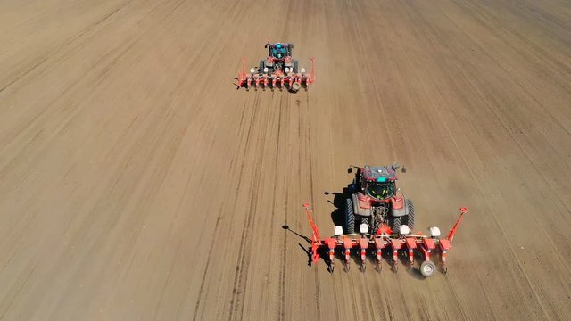 Aerial drone shot of a farmers in two tractor seeding, sowing agricultural crops at field