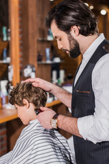 Fototapeta premium adorable curly kid getting haircut from barber with Hair Clipper