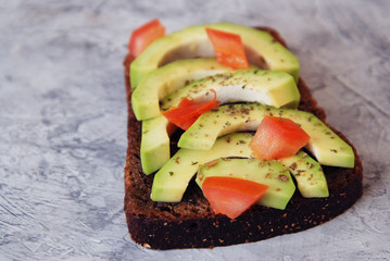 Sliced Avocado on Toast Bread with Spices and tomatoes on a skratched Gray Board. Diet Healthy Fitness Vegan Food