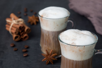 Coffee with rich milk foam in a glass beaker on a dark background sticks of cinnamon and stars of anise. Copy space